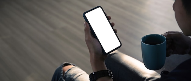 L'immagine mockup dell'uomo si diverte a rilassarsi sul divano usando il cellulare e tenendo una tazza di caffè.