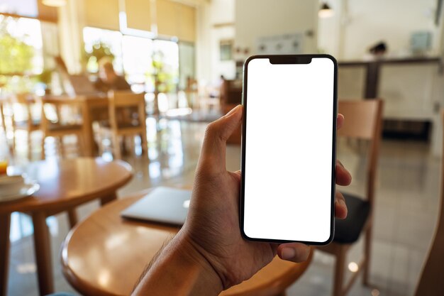 Mockup image of a man holding black mobile phone with blank white screen in cafe