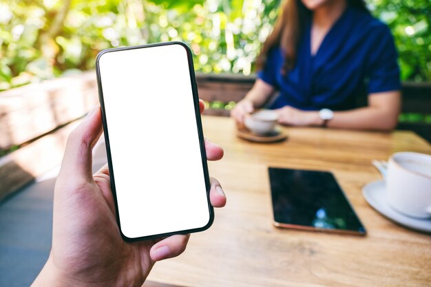 カフェでコーヒーを飲む女性と空白の白い画面で黒い携帯電話を保持している男性のモックアップ画像