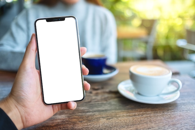 カフェでコーヒーを飲む女性と空白の白い画面で黒い携帯電話を保持している男性のモックアップ画像