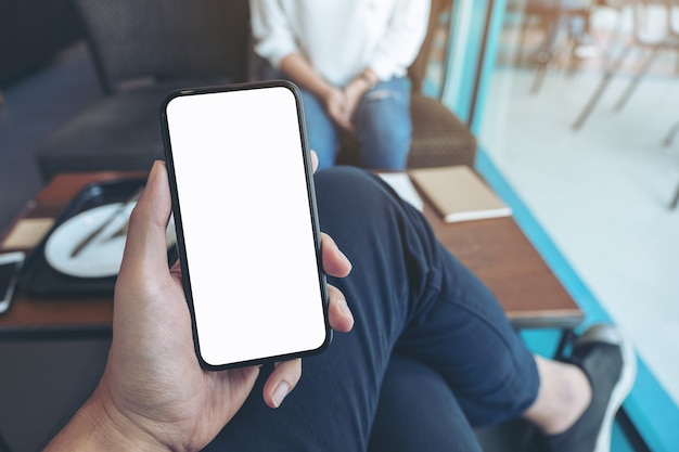 Mockup image of a man holding black mobile phone with blank white screen with woman sitting in cafe