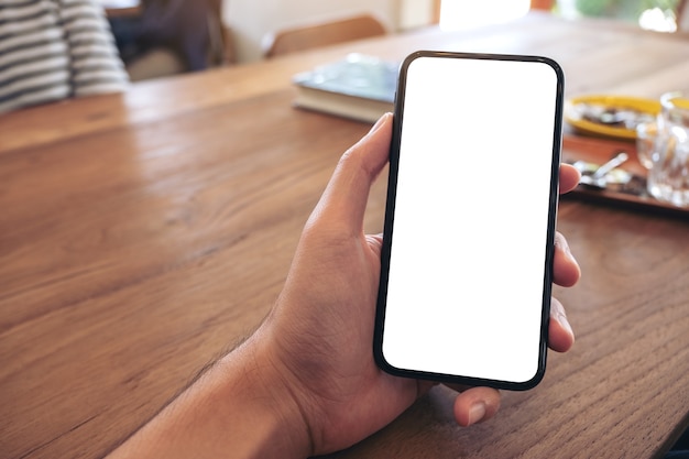 木製のテーブルに空白の画面で黒い携帯電話を持っている男の手のモックアップ画像