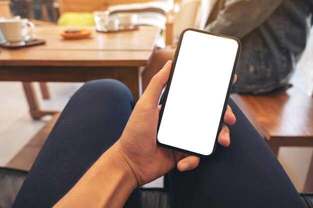 Foto immagine di mockup della mano di un uomo che tiene il telefono cellulare nero con schermo bianco vuoto con la donna che si siede nella caffetteria