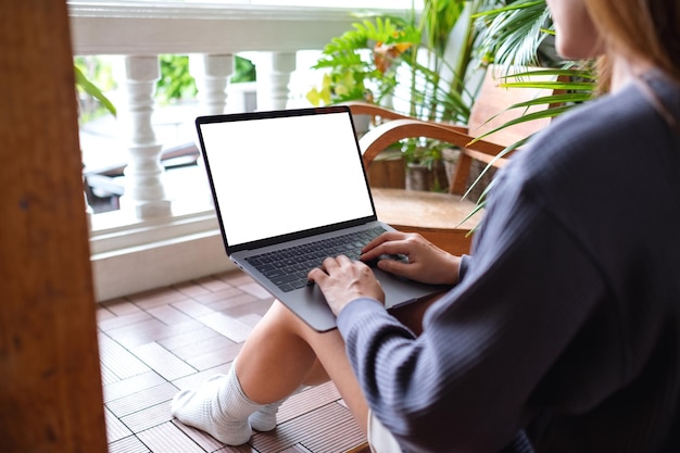집에 있는 발코니에 앉아 있는 동안 빈 흰색 데스크탑 화면이 있는 랩톱 컴퓨터를 사용하고 작업하는 여성의 흉내낸 이미지
