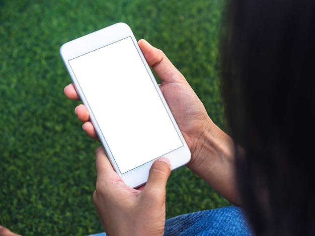 Mockup image of phone. Close-up white blank screen on mobile phone in hands on green artificial grass background. Hand holding white smartphone with empty screen.