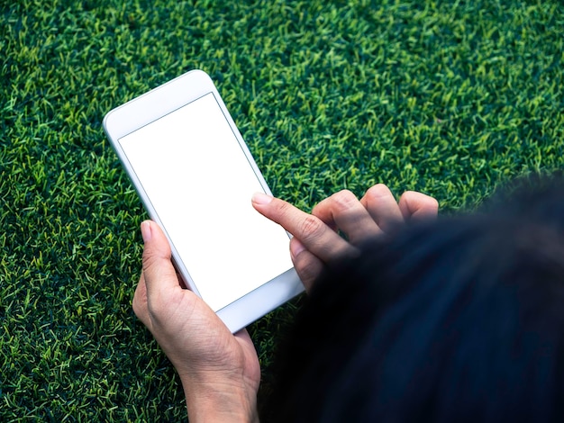 Mockup image of phone. Close-up white blank screen on mobile phone in hands on green artificial grass background. Hand holding white smartphone with empty screen.