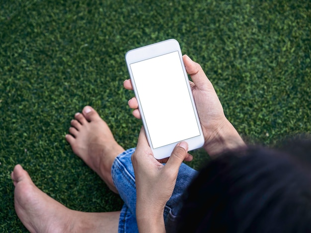 Mockup image of phone. White blank screen on mobile phone in woman hands on green artificial grass background. Hand holding white smartphone with empty screen.