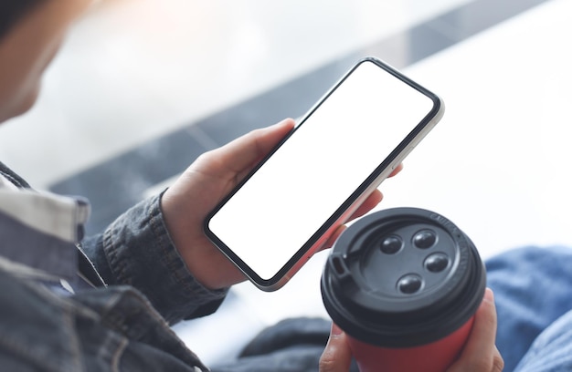 Immagine mockup di mani di donna che tengono il telefono cellulare con schermo vuoto e bevono caffè