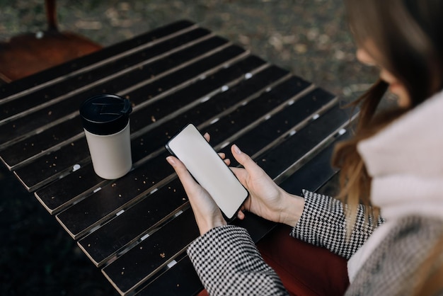 Foto immagine mockup di una donna che tiene un telefono cellulare nero con schermo vuoto con una tazza di caffè sul tavolo