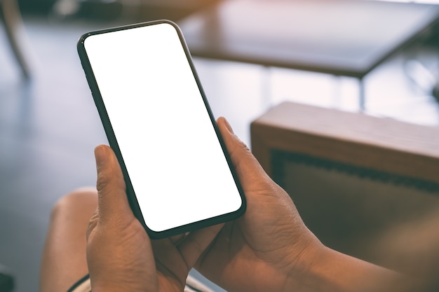 Immagine di mockup di una donna che tiene il telefono cellulare nero con schermo bianco vuoto nella caffetteria