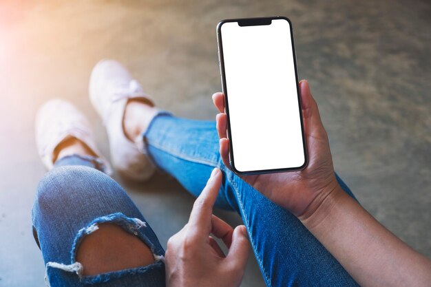 Immagine mockup di una donna che tiene in mano un telefono cellulare nero con schermo bianco vuoto mentre è seduta sul pavimento