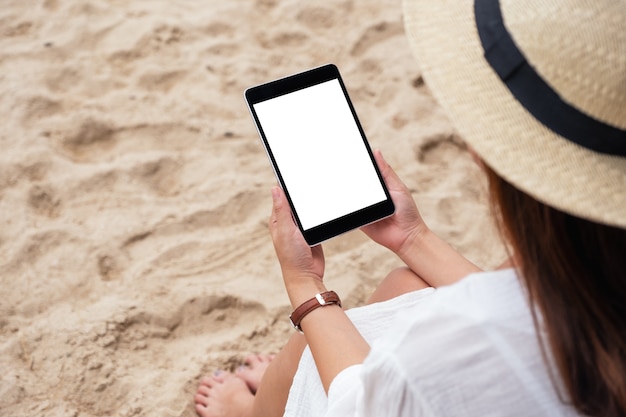 해변 의자에 앉아 있는 동안 빈 데스크탑 화면이 있는 검은색 태블릿 PC를 들고 있는 여성의 모형 이미지