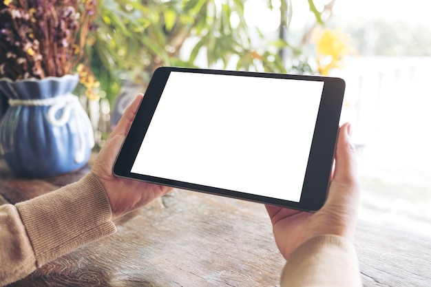 Mockup image of a woman holding black tablet pc with blank white desktop screen in cafe 