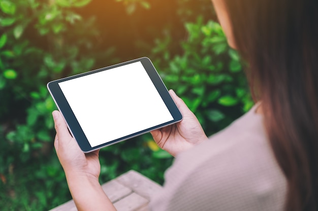 공원에서 빈 흰색 바탕 화면이 있는 검은색 태블릿 PC를 들고 있는 여성의 모형 이미지