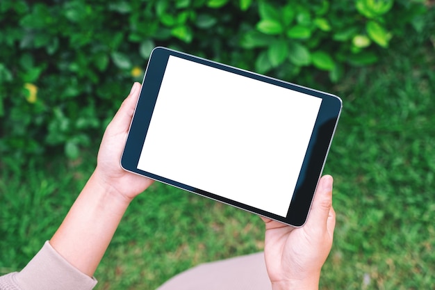 Mockup image of a woman holding black tablet pc with blank white desktop screen in the park