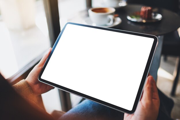 Immagine mockup di una donna che tiene in mano un tablet pc nero con schermo bianco vuoto in un caffè