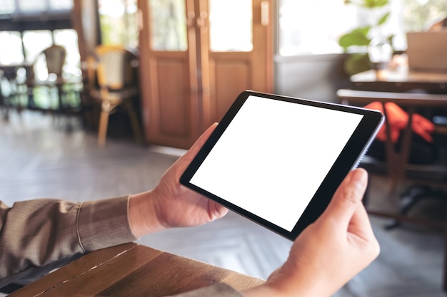 Mockup image of a woman holding black tablet pc with blank white screen horizontally while sitting in cafe