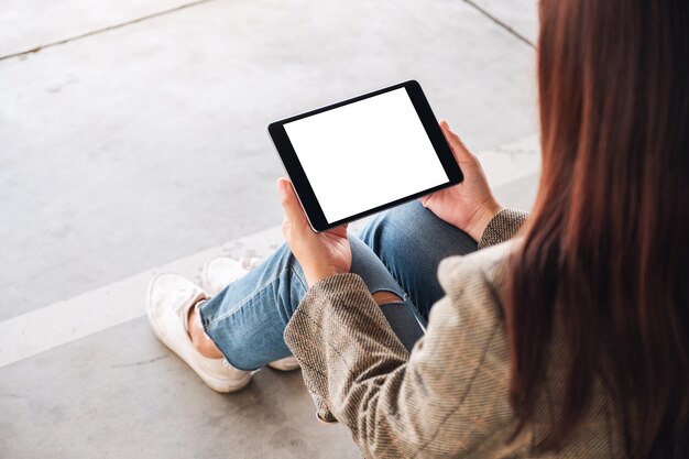 Mockup image of a woman holding black tablet pc with blank white screen while sitting on the floor