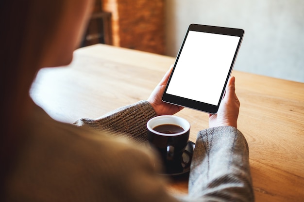 Mockup image of woman holding black tablet pc with blank white screen with coffee cup on wooden table