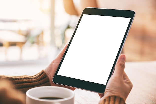 Mockup image of a woman holding black tablet pc with blank white screen with coffee cup on wooden table