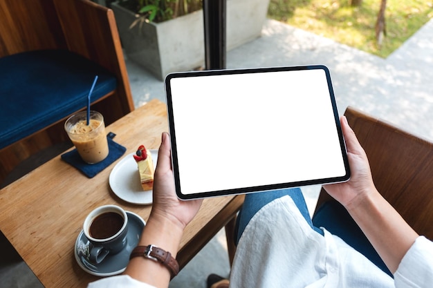 Mockup image of a woman holding digital tablet with blank white desktop screen in cafe