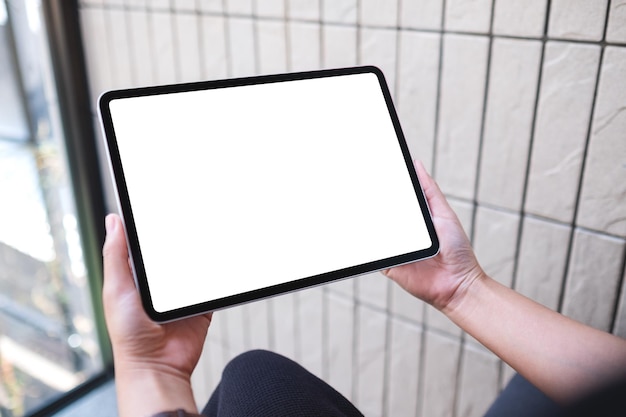 mockup image of a woman holding digital tablet with blank white desktop screen in cafe