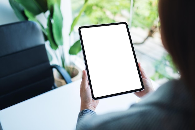 Mockup image of a woman holding digital tablet with blank white desktop screen in the office