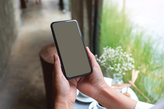 Mockup image of a woman holding mobile phone with blank desktop screen in cafe