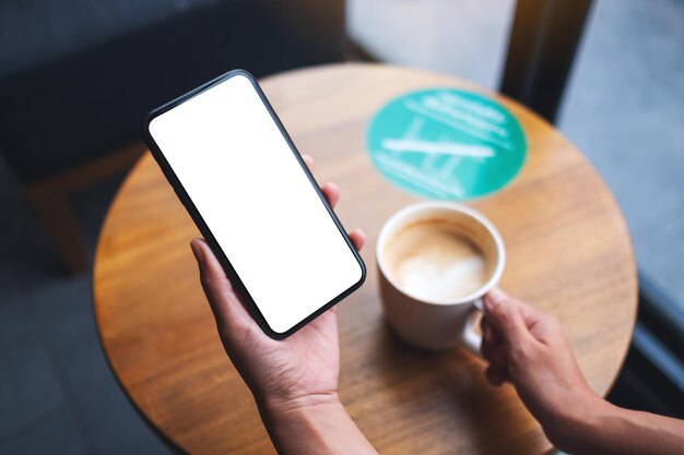 Immagine mockup di una donna che tiene il telefono cellulare con lo schermo del desktop bianco vuoto mentre beve il caffè