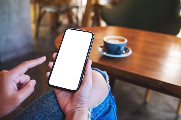 Mockup image of a woman holding mobile phone with blank white desktop screen with coffee cup on wooden table