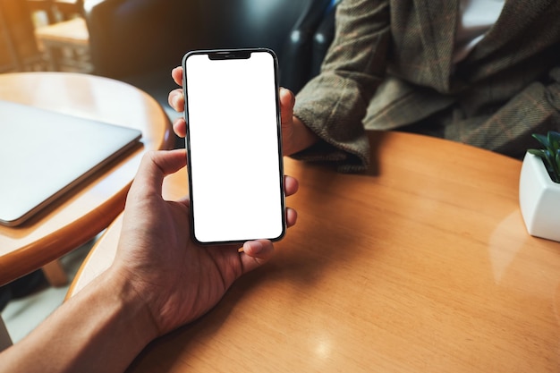 Mockup image of a woman holding and showing mobile phone with blank white desktop screen to someone