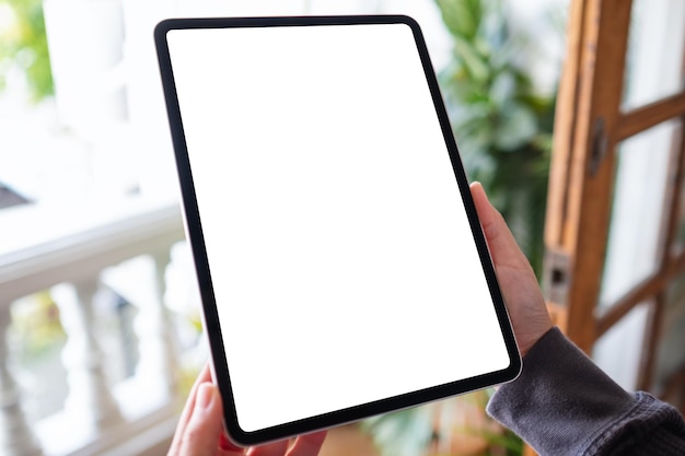 Mockup image of a woman holding and using digital tablet with blank white desktop screen on balcony at home