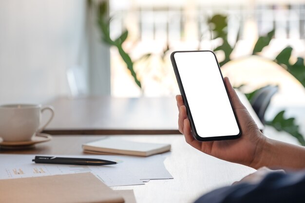 Mockup image of a woman holding and using mobile phone while working in office