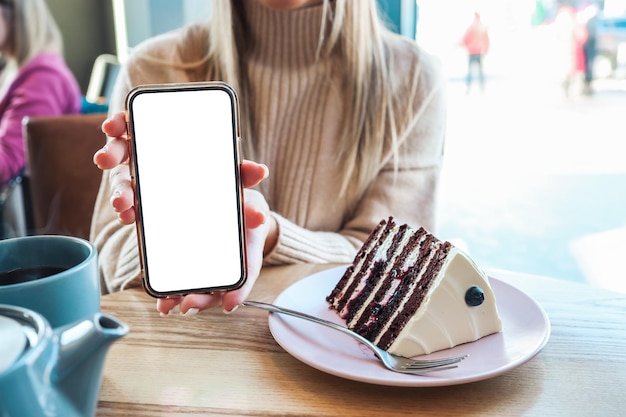 Mockup image of woman holding and using mobile phone with empty desktop space while drinking coffee in cafe