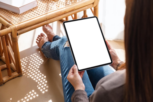 自宅で空白のデスクトップの白い画面でタブレットPCを保持して使用している女性のモックアップ画像