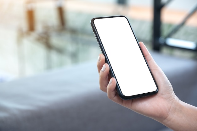 Photo mockup image of a woman's hand holding black mobile phone with blank white desktop screen