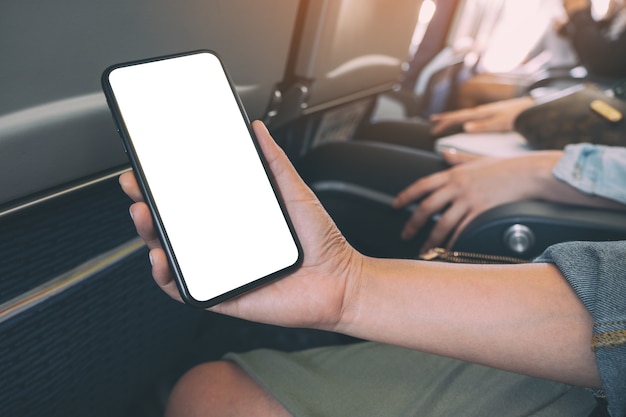 Mockup image of woman's hand holding a black smart phone with blank desktop screen in cabin