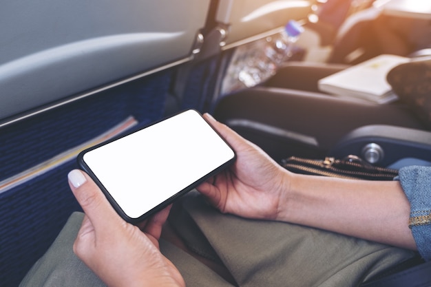 Mockup image of woman's hands holding a black smart phone with blank desktop screen horizontally in cabin