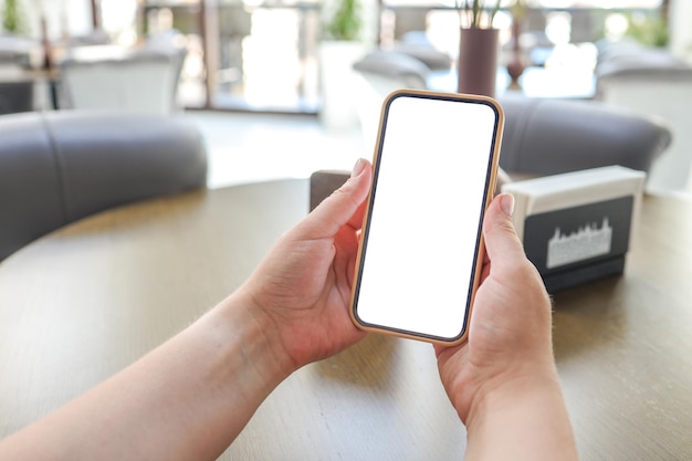 Immagine mockup delle mani della donna che tengono il telefono cellulare bianco con lo schermo vuoto nella caffetteria