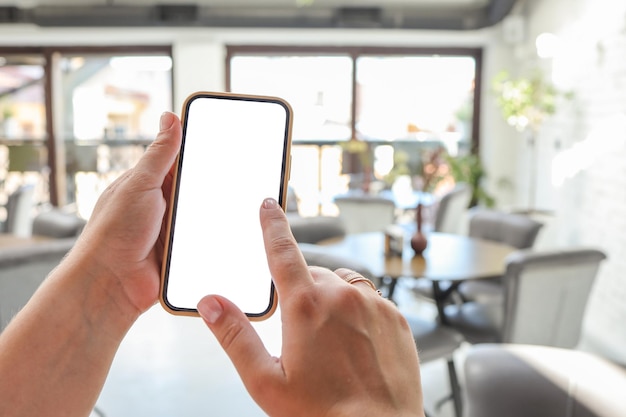 カフェで空白の画面と白い携帯電話を保持している女性の手のモックアップ画像