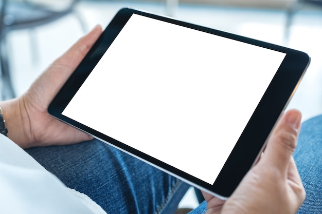 Mockup image of a woman sitting and holding black tablet pc with blank white desktop screen horizontally