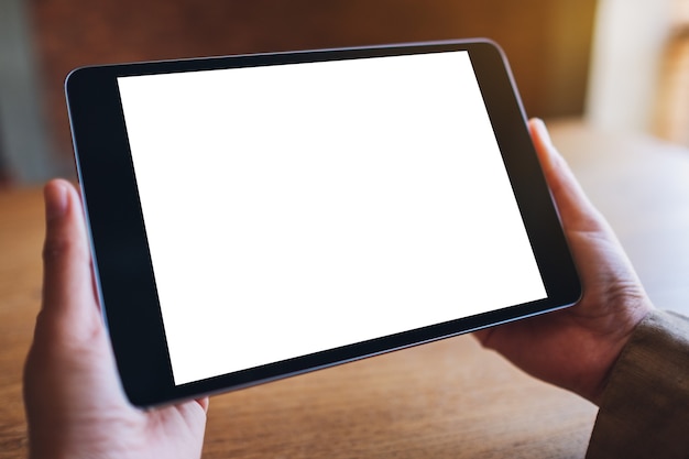 Mockup image of a woman sitting and holding black tablet pc with blank white desktop screen