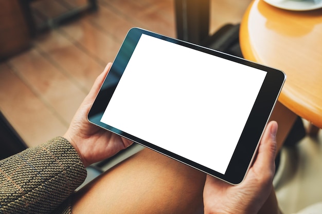 Mockup image of a woman sitting and holding black tablet pc with blank white desktop screen