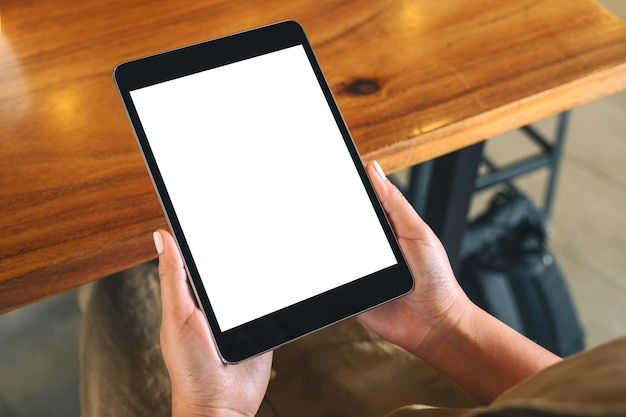 Mockup image of a woman sitting and holding black tablet pc with blank white desktop screen