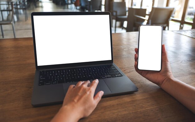 Mockup image of a woman touching on laptop touchpad with blank white desktop screen while using mobile phone