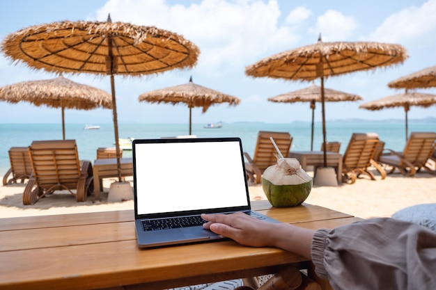 Mockup image of a woman using and touching on laptop touchpad with blank desktop screen while sitting on the beach