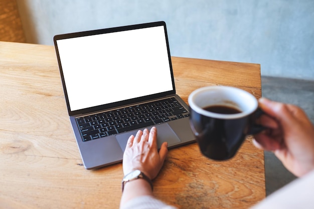 Mockup image of a woman using and touching on laptop touchpad with blank white desktop screen while drinking coffee in cafe