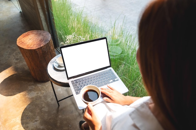 Mockup image of a woman using and touching on laptop touchpad with blank white desktop screen while drinking coffee in cafe