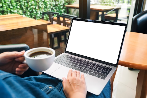 Immagine mockup di una donna che usa e tocca il touchpad del laptop con uno schermo desktop bianco vuoto mentre beve caffè