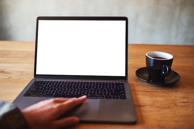 Immagine mockup di una donna che usa e tocca il touchpad del laptop con uno schermo desktop bianco vuoto con una tazza di caffè sul tavolo